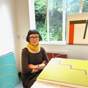 UGallery artist Shyun Song sitting in her studio, surrounded by her abstract paintings