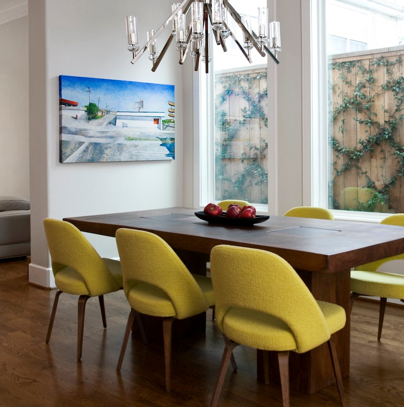 Client dining room with wooden table and yellow chairs, featuring a landscape painting by artist Mitchell Freifeld.