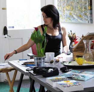  Artist Lisa Elley working on her painting in her well-lit studio filled with art supplies 