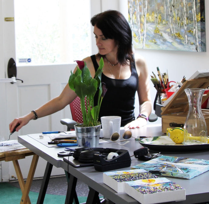  Artist Lisa Elley working on her painting in her well-lit studio filled with art supplies 