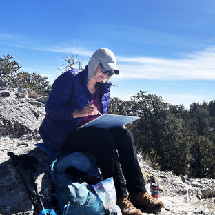  UGallery artist Crystal DiPietro sitting on a rock while painting en plein air 