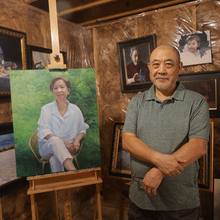  UGallery artist Shuxing Fan in his studio beside a portrait painting of a woman 