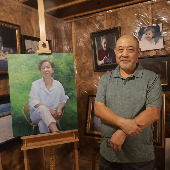  UGallery artist Shuxing Fan in his studio beside a portrait painting of a woman 