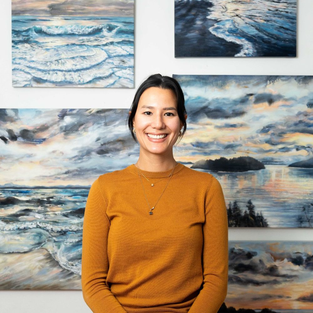  UGallery artist Tiffany Blaise in front of a gallery wall with her seascape paintings 